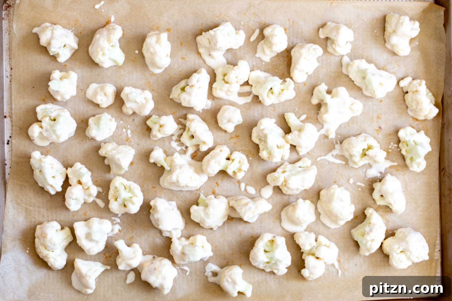 Battered cauliflower florets arranged in a single layer on a parchment-lined baking sheet, ready to go into the oven.