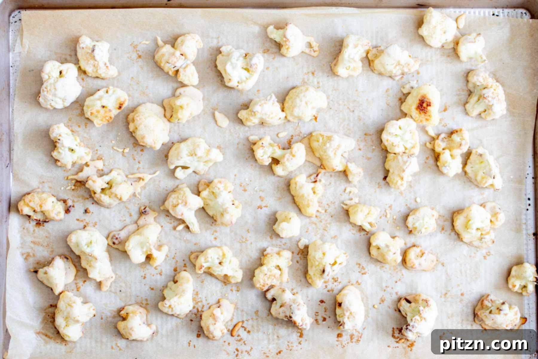 Golden-brown and crispy baked cauliflower florets cooling on the baking sheet after being removed from the oven.