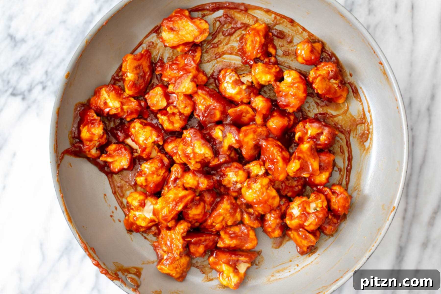 Cauliflower florets completely coated in the vibrant red gochujang sauce, mixed thoroughly in the pan.