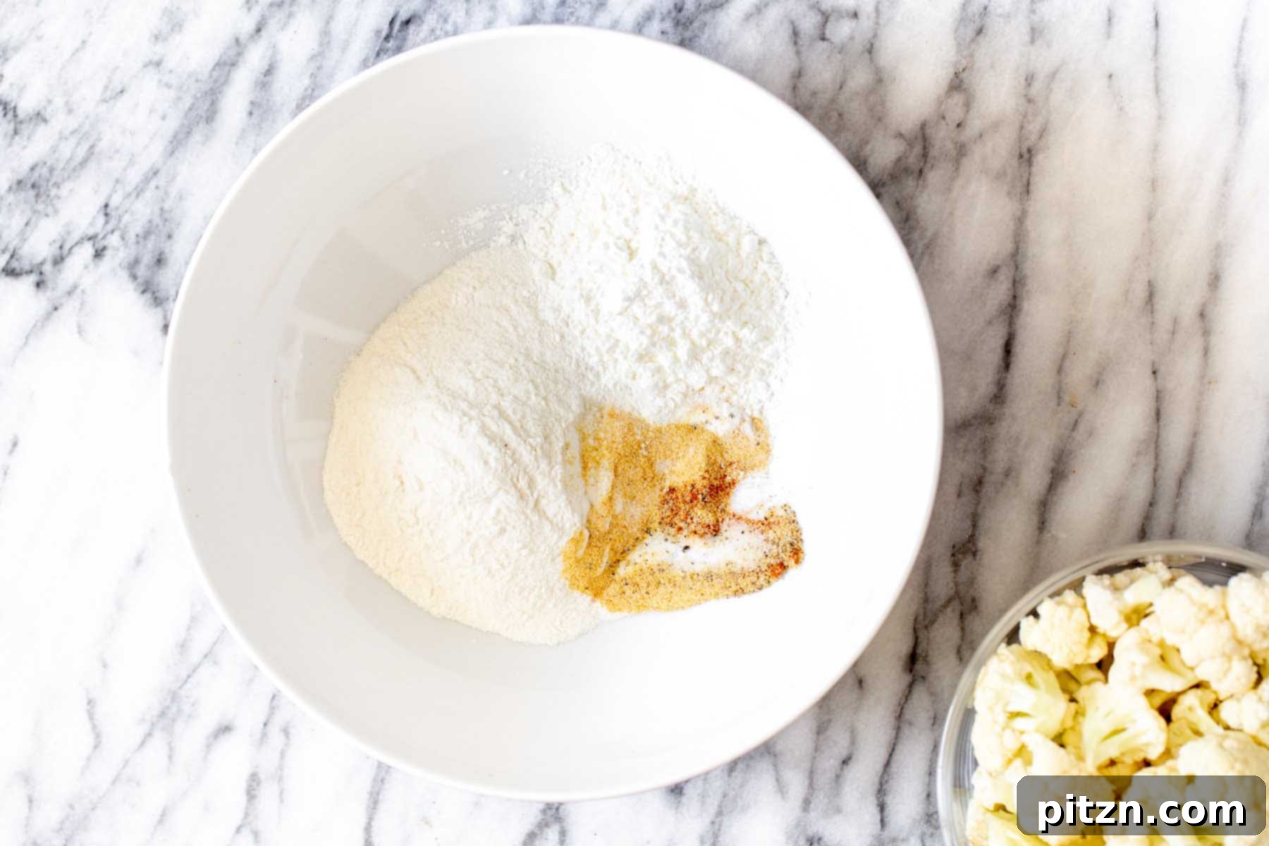 Dry ingredients for cauliflower batter, including rice flour, tapioca starch, and spices, measured out in a bowl before mixing.