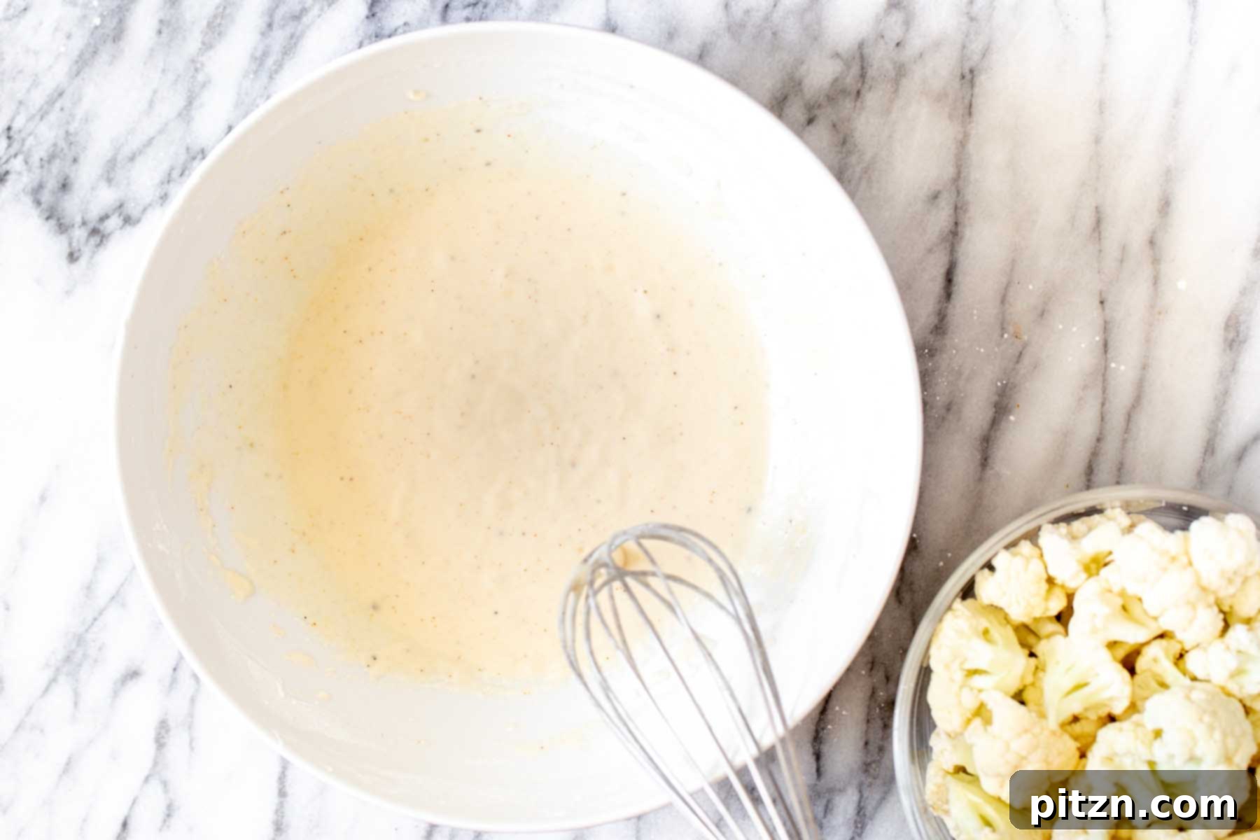 The smoothly mixed cauliflower batter in a bowl, showcasing its ideal consistency after all ingredients have been combined.