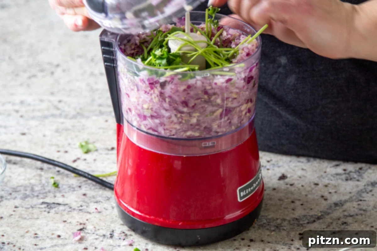Vegan Lentil Keema Pav Bake 8 adding cilantro stems to chopped onions, garlic, ginger, and chili in a food processor
