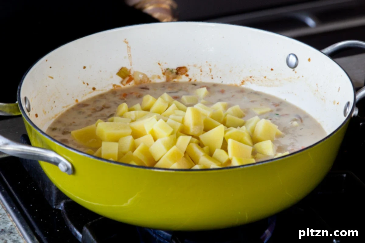 Fireside Smoked Potato Soup 14 Cubed potatoes being added to the creamy soup base in the pan, ready to be cooked until tender
