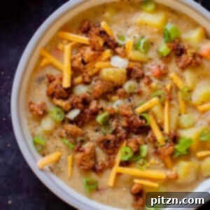 Bowl of smoky vegan potato soup topped with tofu crumbles, green onions, and vegan cheese