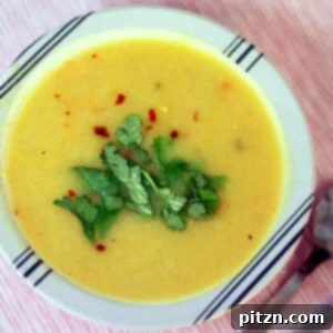 A bowl of carrot, leek, and parsnip soup garnished with green leaves, ready to be served.