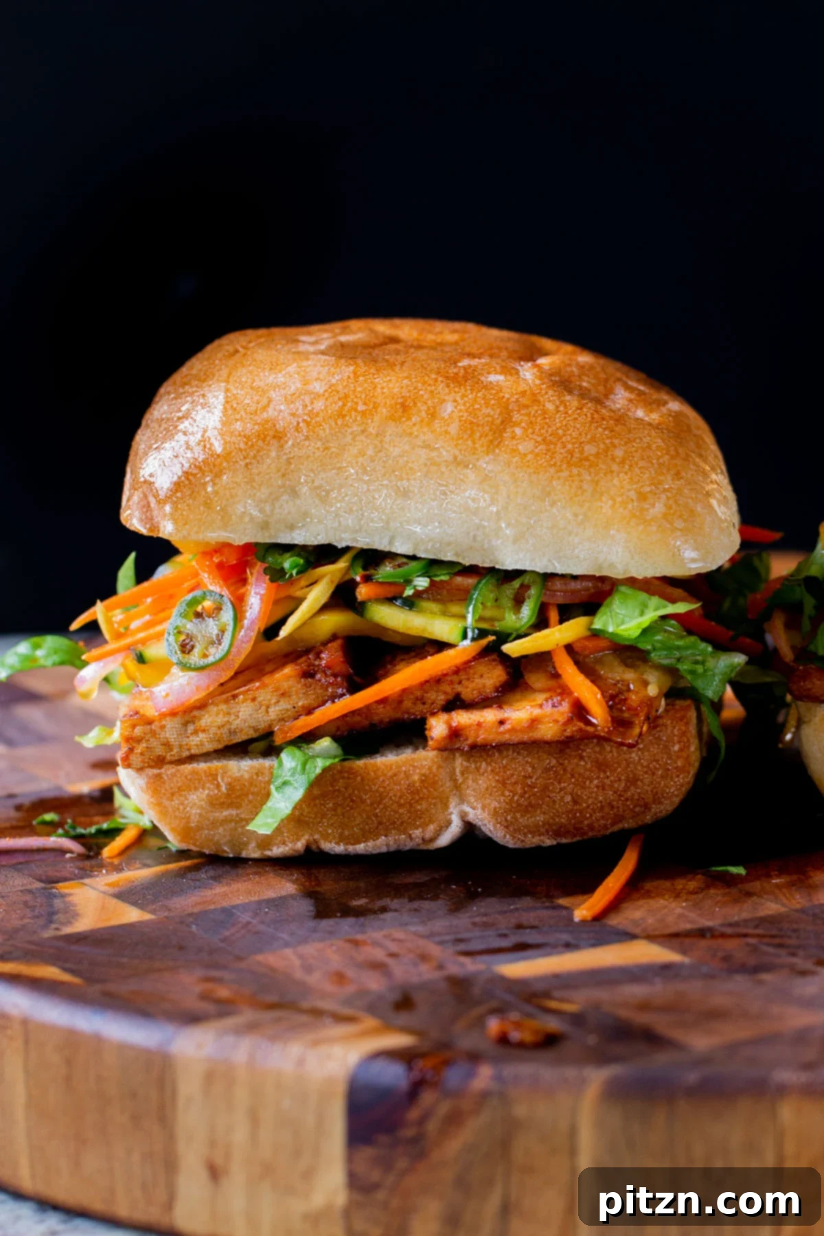 Spicy Gochujang Tofu Sandwich 2 Gochujang tofu banh mi with pickled veggies on a wooden cutting board, showcasing the vibrant colors and textures.