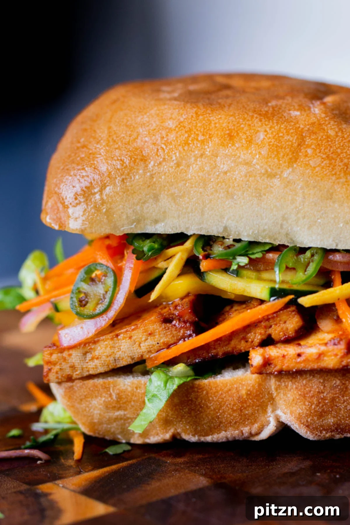 Spicy Gochujang Tofu Sandwich 4 Close-up of a gochujang sandwich with pickled veggies on a wooden cutting board, highlighting the fresh ingredients.