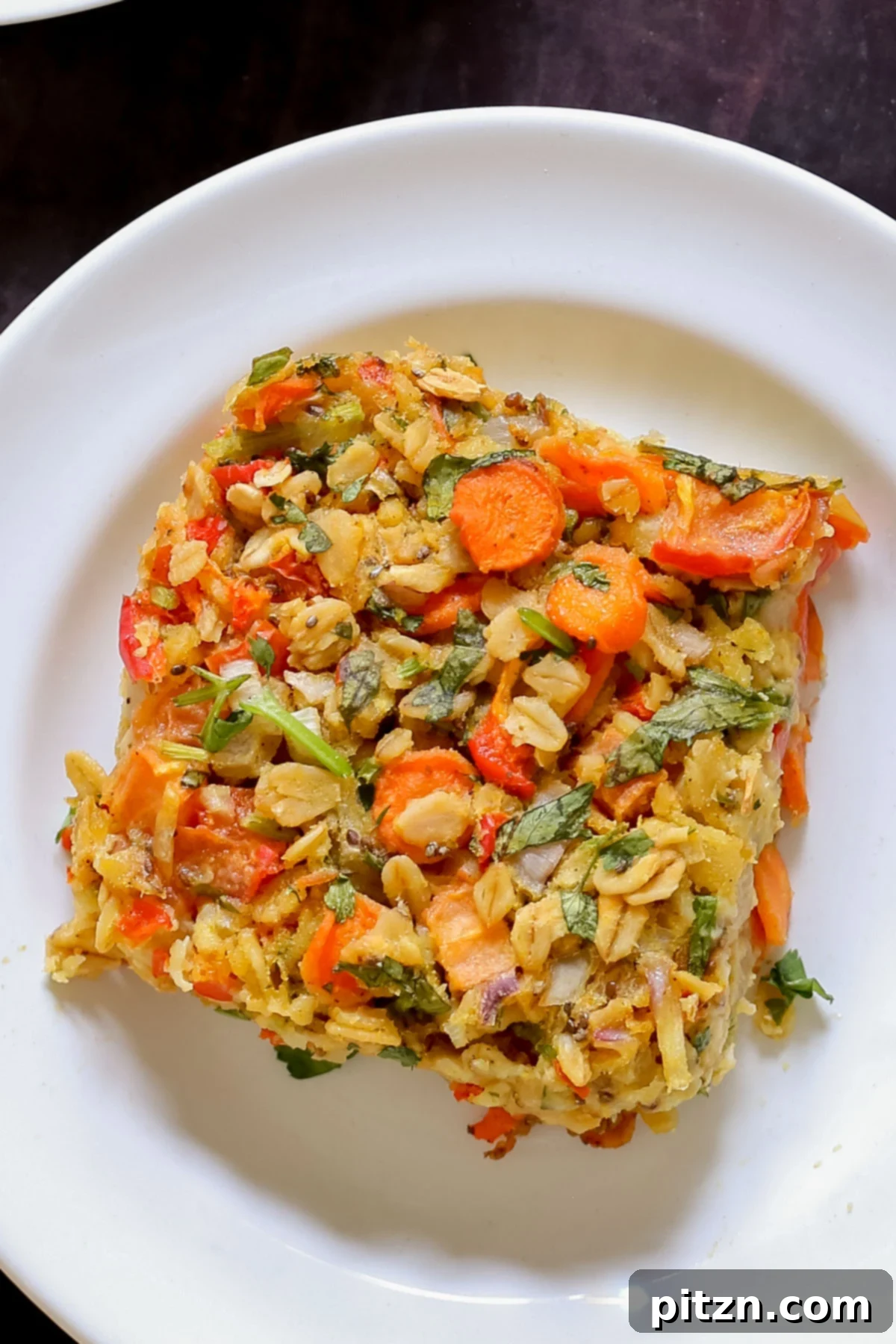 Vegan Savory Vegetable Baked Oats 4 close-up of a piece of savory baked oatmeal on a white plate, highlighting the texture and embedded vegetables