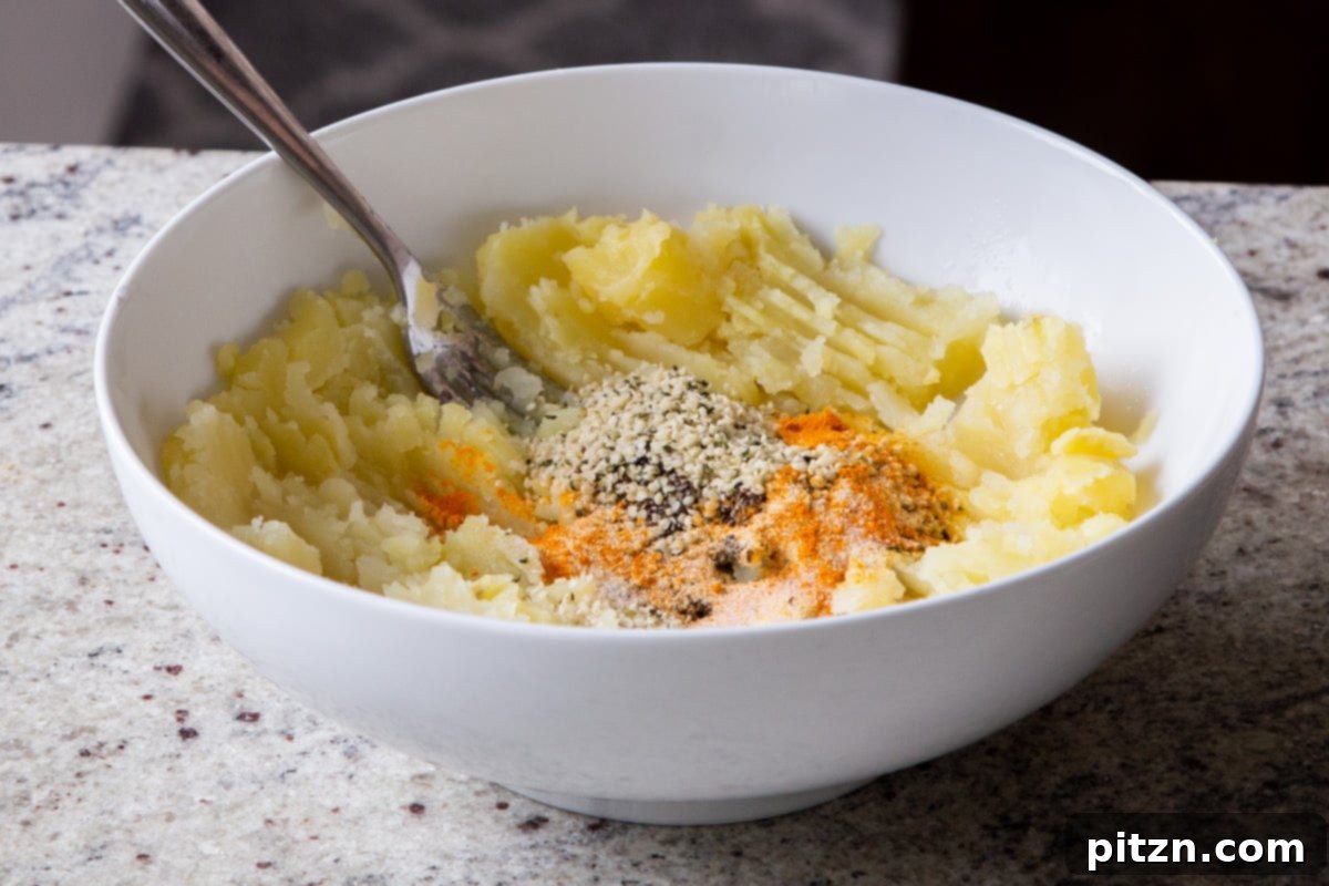 Various spices and seeds being sprinkled into a bowl of mashed potatoes, ready to be mixed into the flavorful filling.