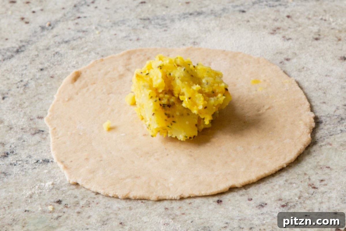 A rolled-out paratha dough circle with a mound of spiced potato filling precisely placed in its center.