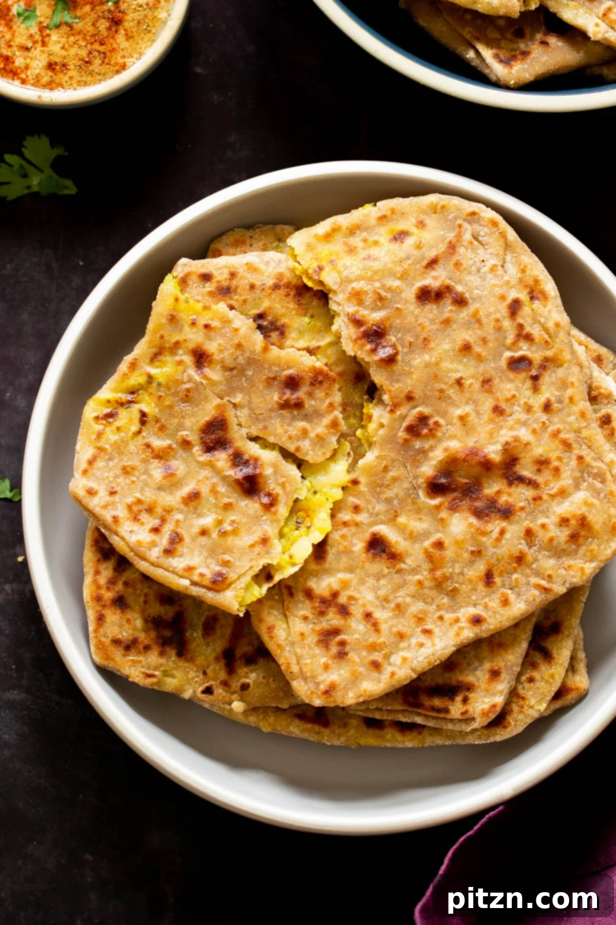A freshly cooked multigrain aloo paratha torn open, revealing the vibrant, spiced potato filling inside, stacked on a plate.