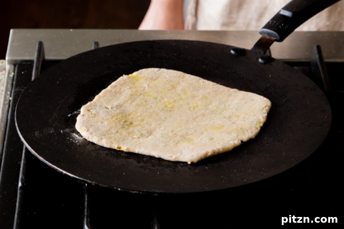 A multigrain aloo paratha cooking on a hot skillet, with a light browning visible on its surface.