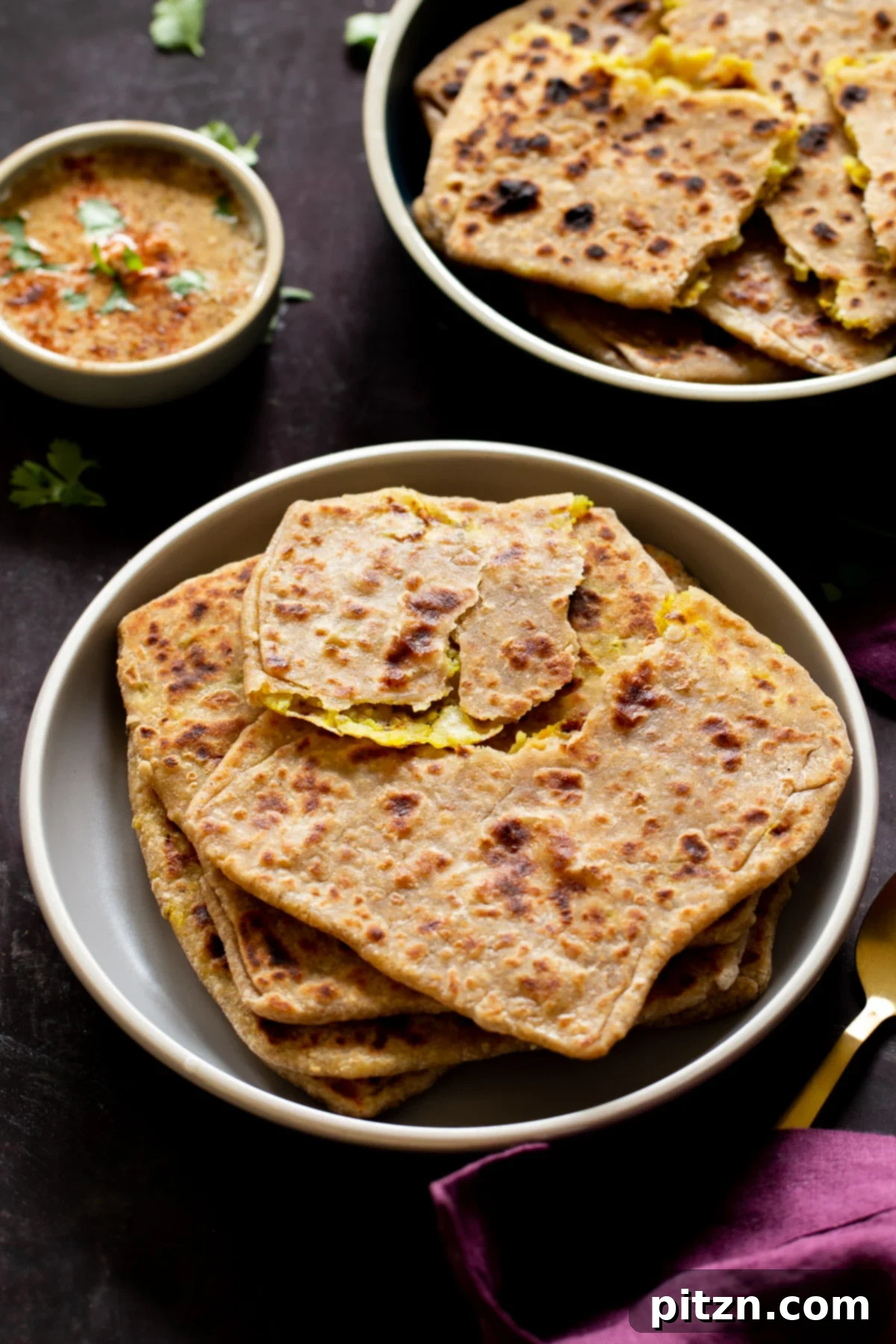 An array of freshly prepared multigrain aloo parathas arranged beautifully on serving platters, accompanied by various vibrant chutneys for dipping.