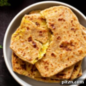 aloo paratha pilled up on a plate, top one is torn open, so you can see the filling
