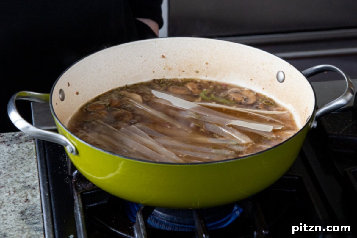 Hearty One-Pot Mushroom Noodle Delight 15 Rice noodles being added to the simmering pan of broth and mushrooms, ready to cook.