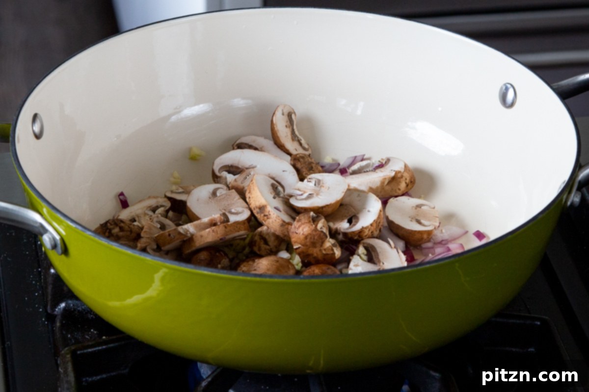 Hearty One-Pot Mushroom Noodle Delight 9 Sliced mushrooms being added to the pan with sautéed onion and garlic, ready to be cooked down.