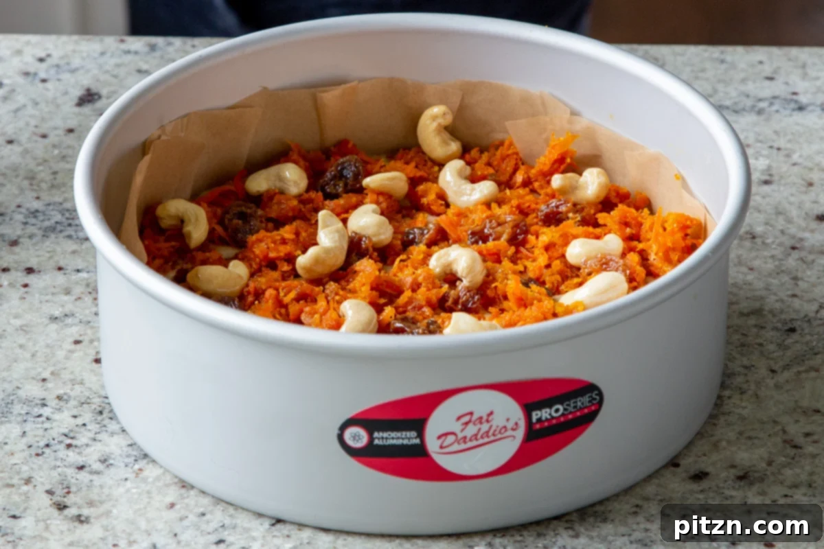 Decadent Carrot Halwa Gateau 27 Cashews and raisins are carefully arranged and pressed into the carrot mixture on top of the cake pan, ready for baking.