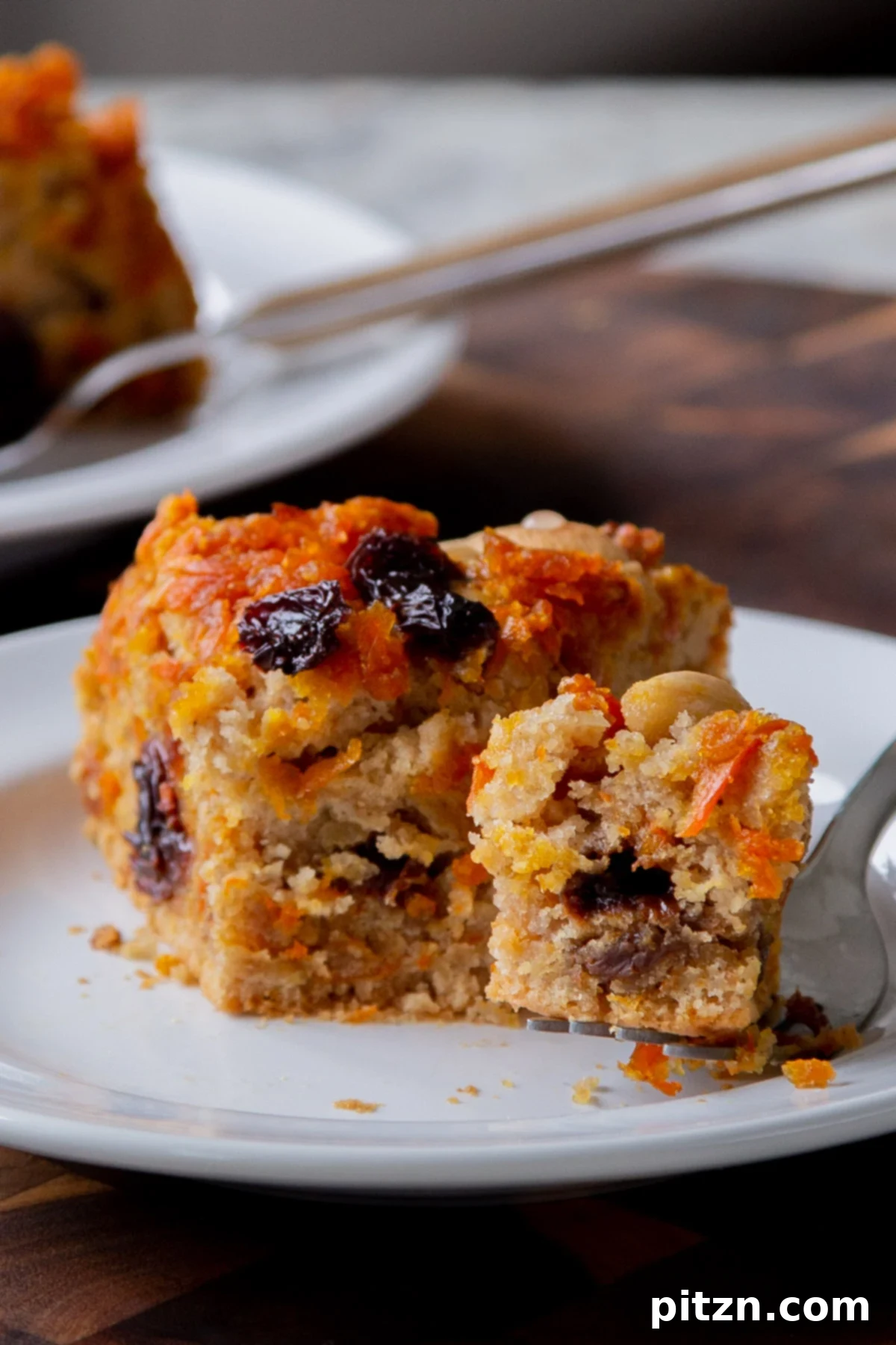 Decadent Carrot Halwa Gateau 5 A delectable slice of vegan carrot halwa cake on a white plate, with a small bite taken out, revealing its soft interior.