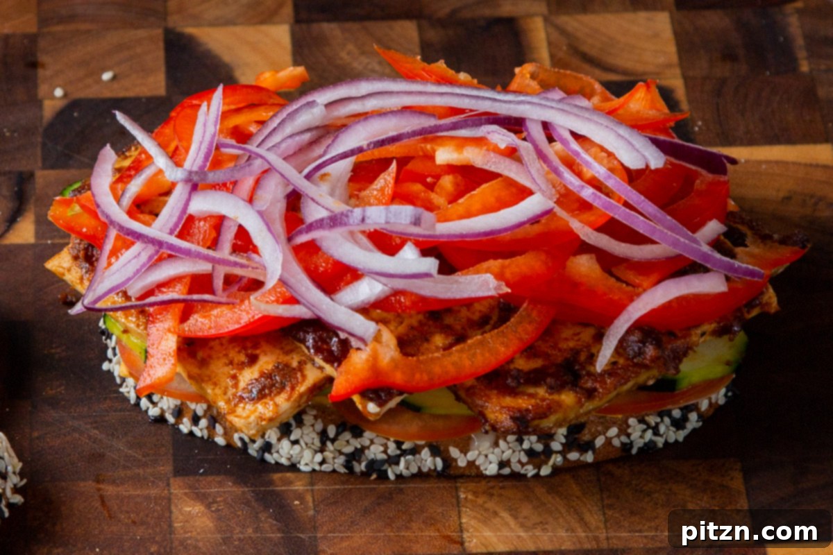 Plant-Based Deli Club 16 Thinly sliced red onion and vibrant red bell pepper being layered onto the sandwich, adding color and crunch to the fillings.