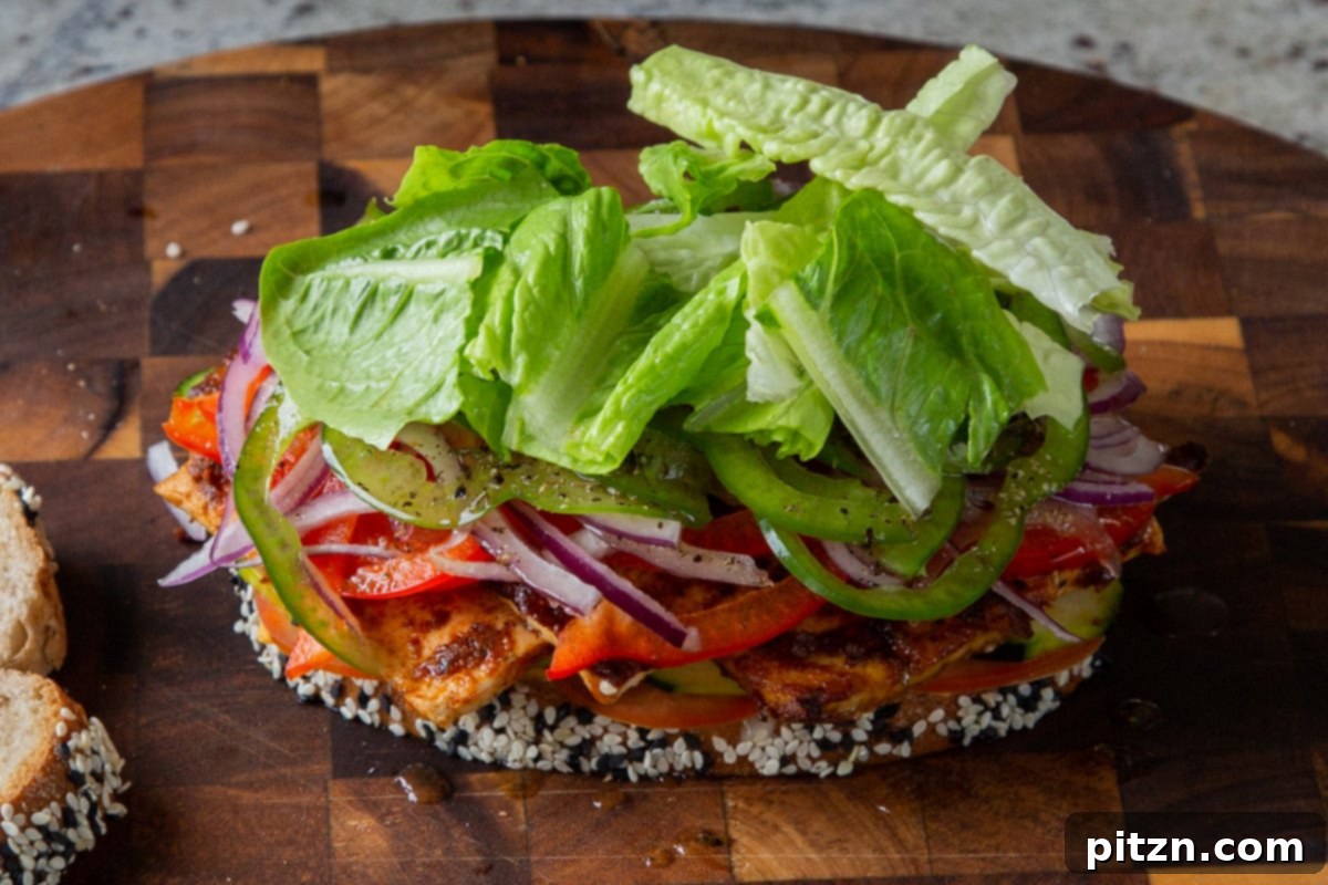 Plant-Based Deli Club 18 Fresh lettuce leaves and a drizzle of vinaigrette being added to the top layer of vegetables, preparing the sandwich for its final slice of bread.