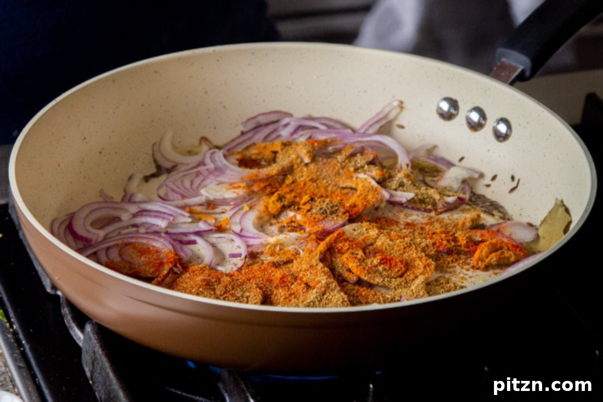 The process of adding thinly sliced onions and a colorful array of ground spices to the frying pan, where cumin seeds are already toasted, for the Ghugni sauce base.