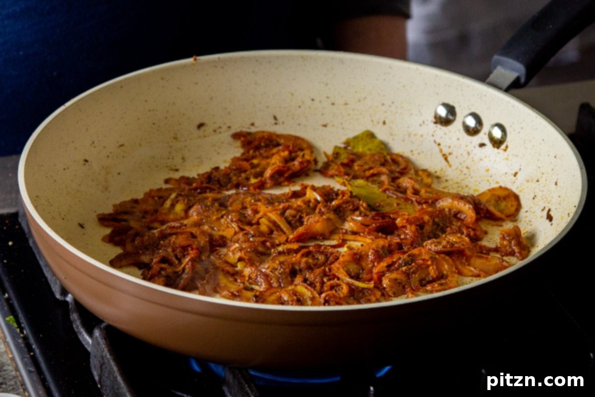 Close-up of perfectly sautéed golden and caramelized onions in the frying pan, forming the rich base for the Ghugni sauce, ready for the next ingredients.