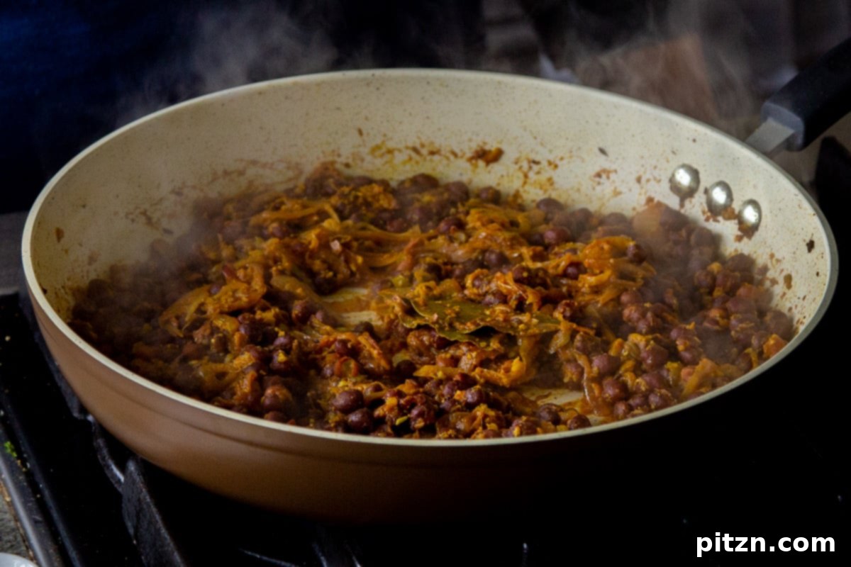 The fully cooked Kala Chana Ghugni, vibrant with spices and chickpeas, simmering gently in the frying pan, with flavors perfectly melded.