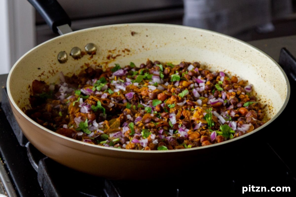 Beautifully garnished Kala Chana Ghugni with a generous topping of fresh onions and vibrant cilantro, still in the frying pan, ready to be presented.