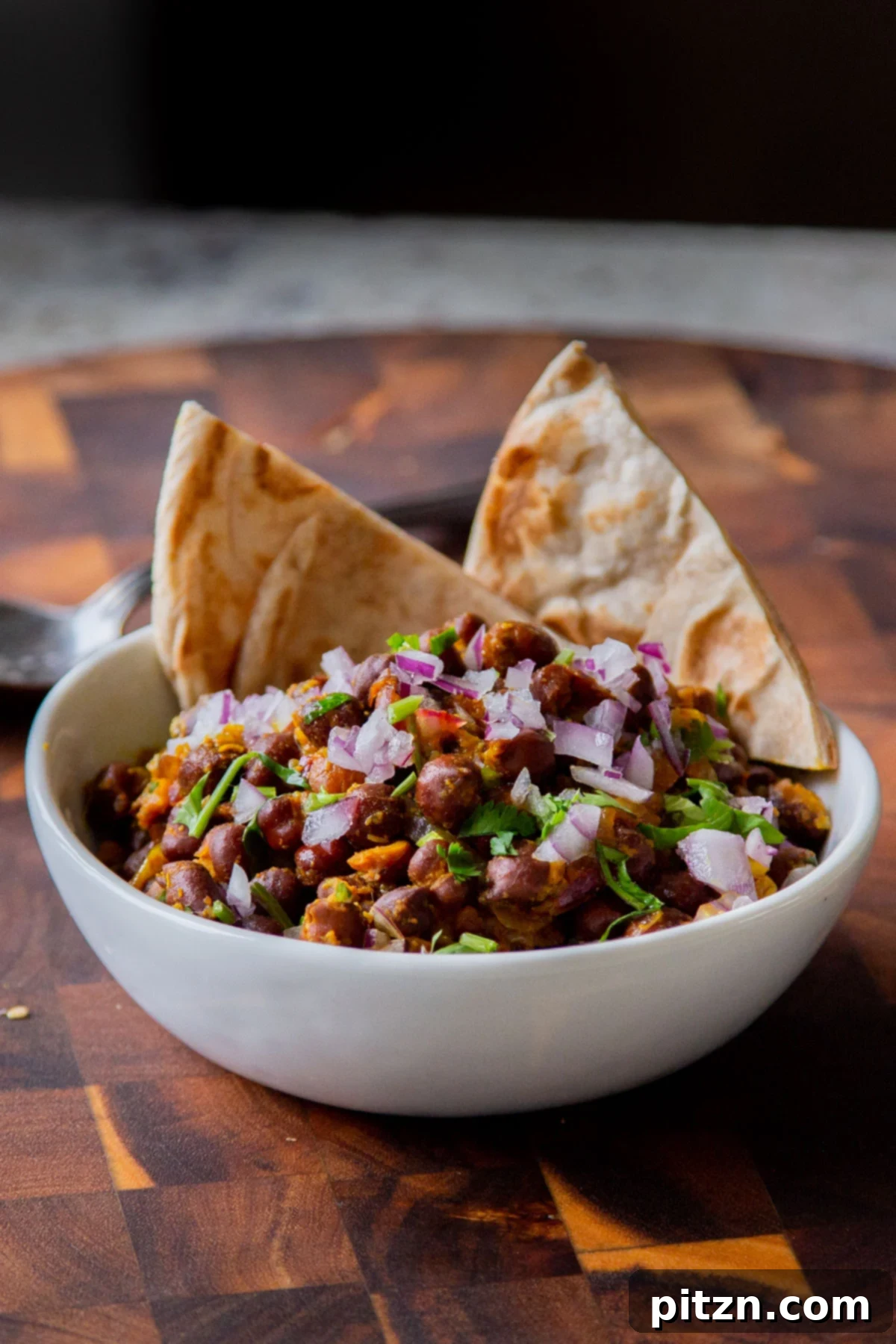 A delicious bowl of Kala Chana Ghugni, garnished with crisp onions, fresh cilantro, and cumin, served alongside warm flatbread.