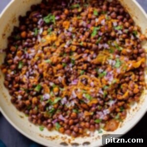 Kala Chana Ghugni (Brown Chickpea Curry) in a frying pan, garnished with fresh herbs and onions, ready to serve.
