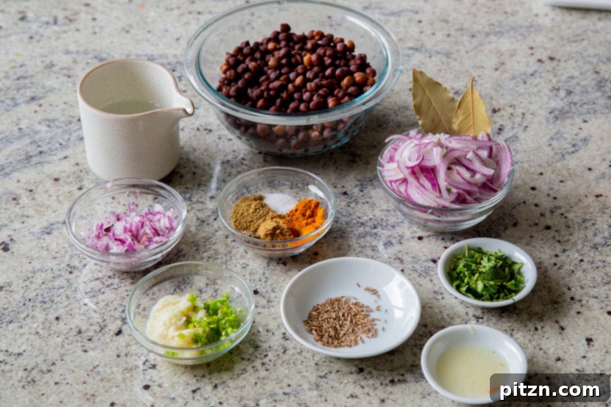 A collection of raw brown chickpeas, fresh vegetables including onions and green chilies, and an array of vibrant Indian spices laid out in bowls on a kitchen counter, showcasing the fresh ingredients for making Ghugni.