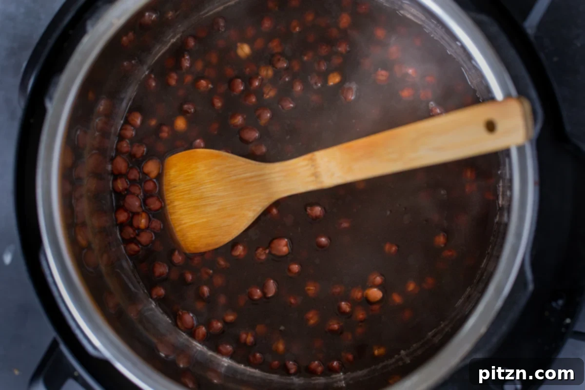 Cooked brown chickpeas settled at the bottom of the Instant Pot, with residual cooking water, after the pressure has been safely released.