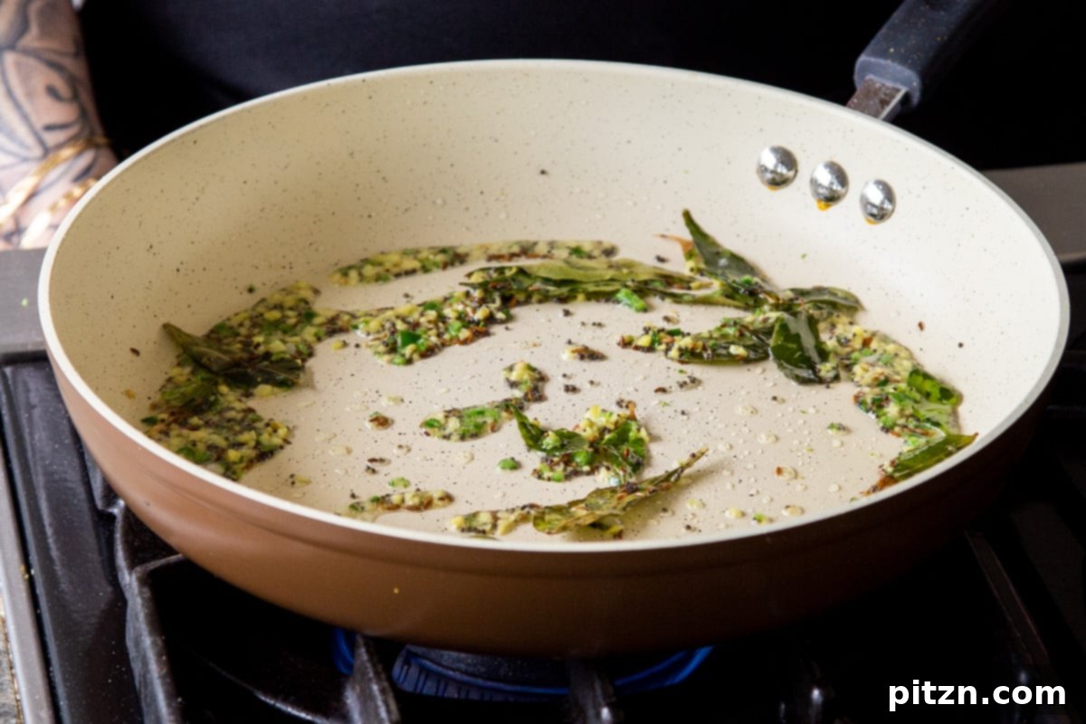 Ginger, green chili, and whole spices sizzling in the pan after being cooked, releasing their pungent and aromatic flavors, a key step for Rava Idli Waffles.