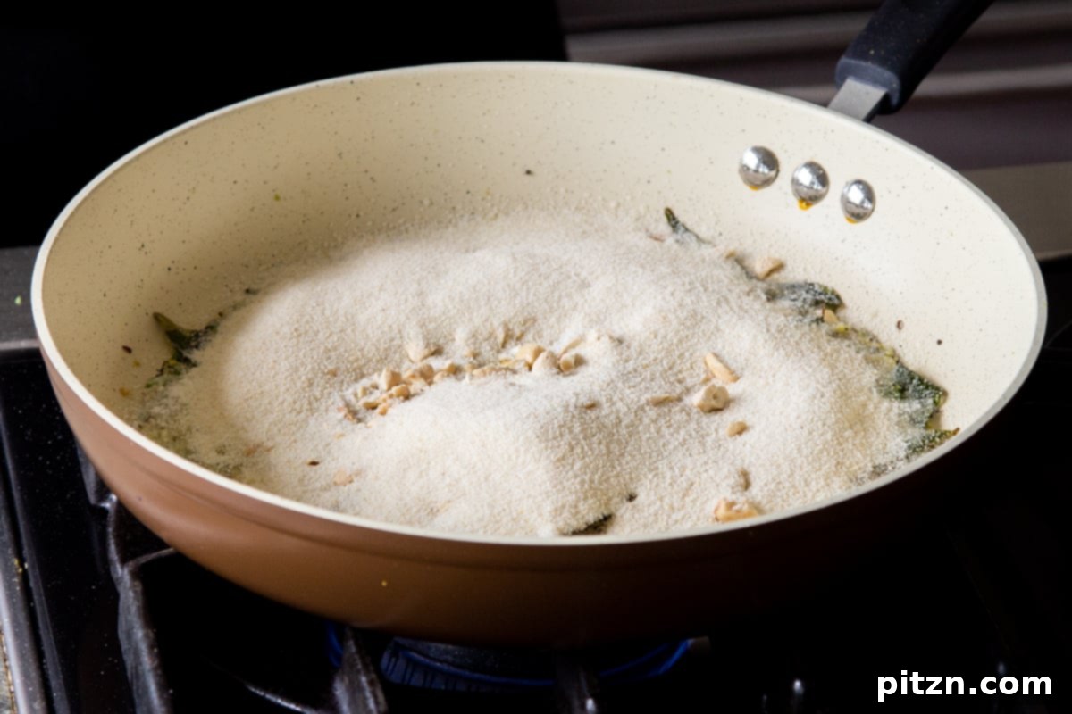 Coarse semolina being added to the pan containing toasted whole spices, ginger, and chili, preparing for roasting to create the base for Rava Idli Waffles.
