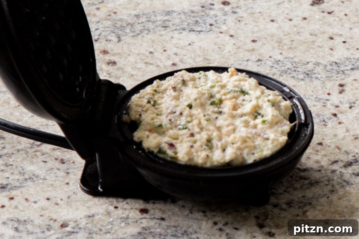 Raw Rava Idli waffle batter placed in a preheated waffle maker, ready to be cooked into a golden, savory waffle.