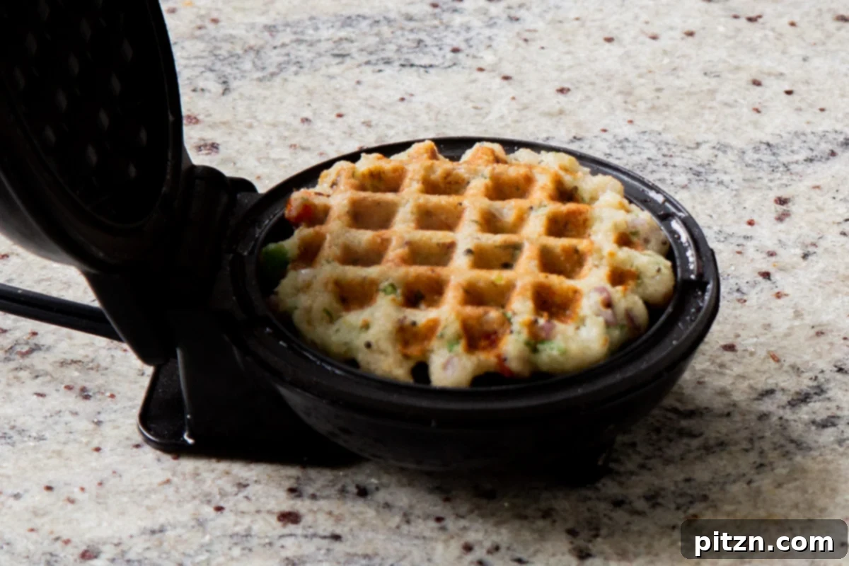 A perfectly cooked, golden brown Rava Idli waffle in the waffle maker, crisp and ready to be served as a savory breakfast.