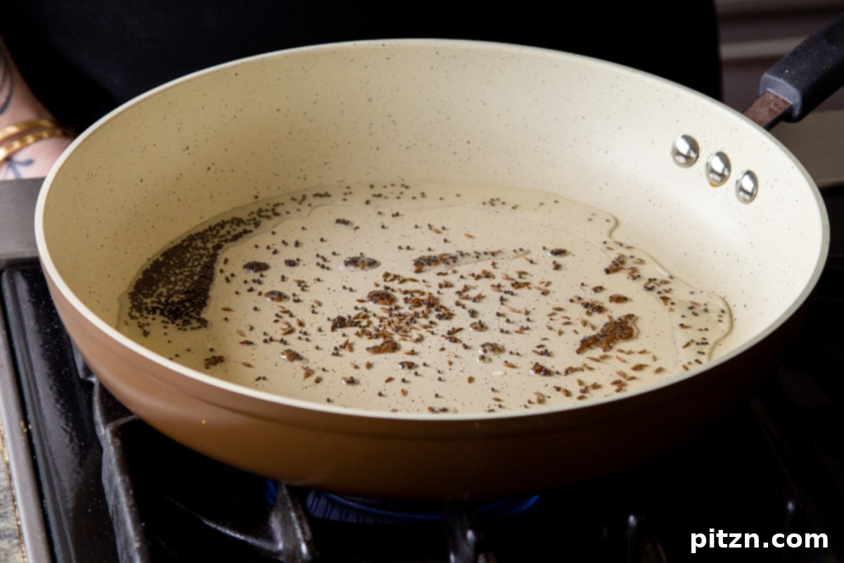 Adding whole mustard and cumin seeds to hot oil in a skillet, capturing the start of tempering for the Rava Idli Waffles.