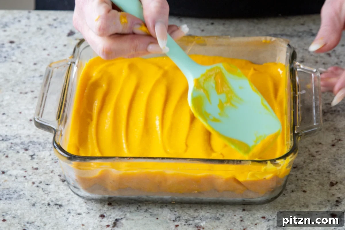 using a spatula to spread the mango custard over the crust