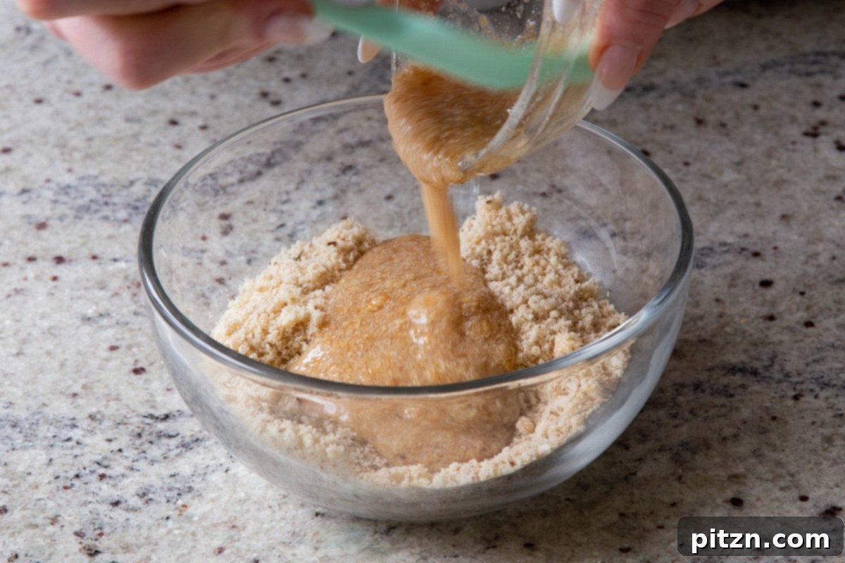 The wet ingredients for the almond flour croutons, including oil and flax egg, being added to the bowl of dry ingredients, ready for mixing to form the dough.