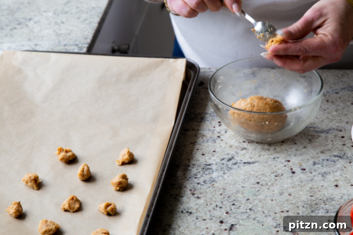 Small portions of almond flour crouton dough being carefully scooped onto a parchment-lined baking sheet, preparing them for baking.