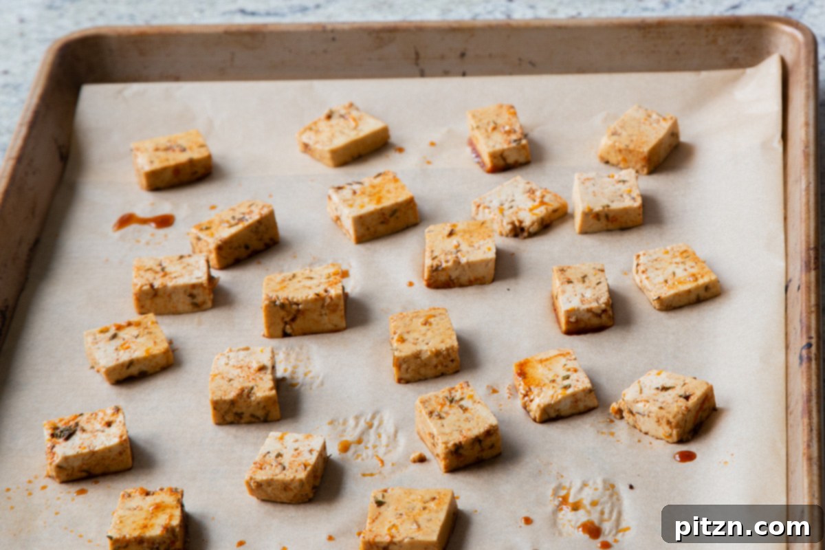 Marinated smoky tofu pieces arranged on a baking sheet lined with parchment paper, ready to be baked until crispy and golden brown.