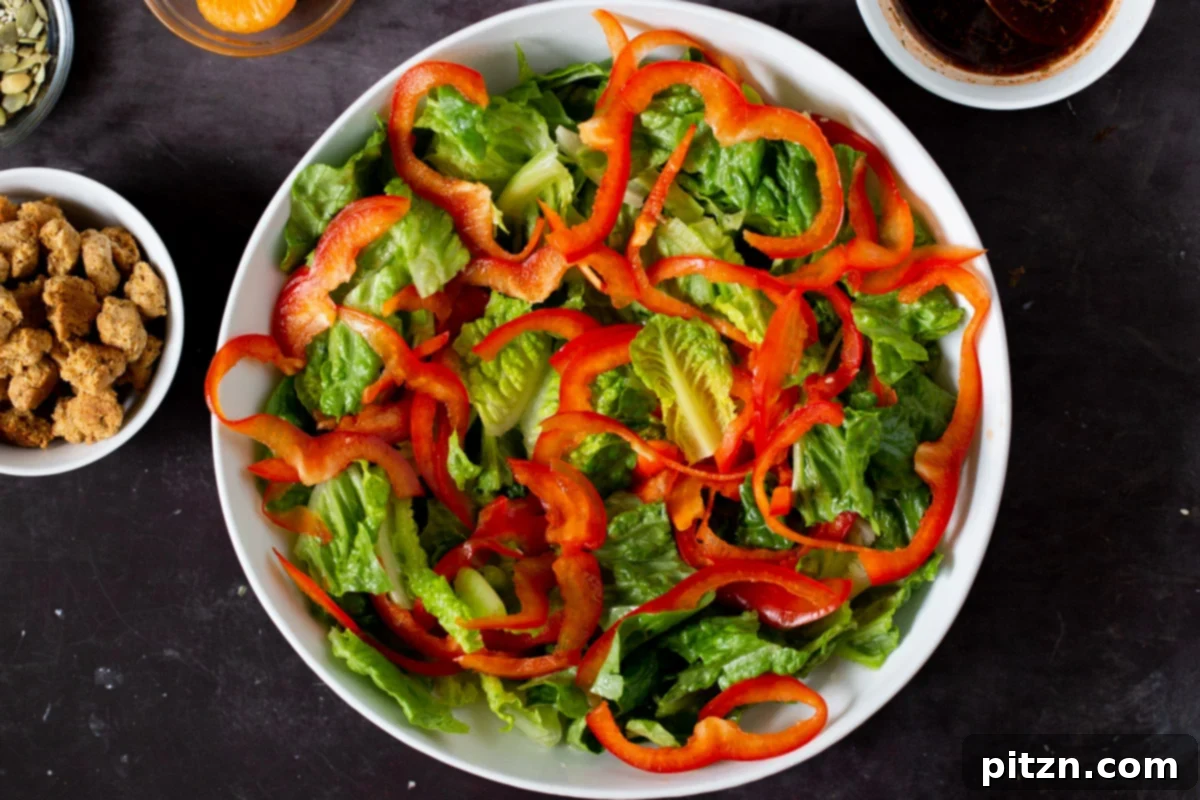 Sliced red bell pepper being added to the bed of lettuce in the salad bowl, introducing a vibrant color and crisp texture.