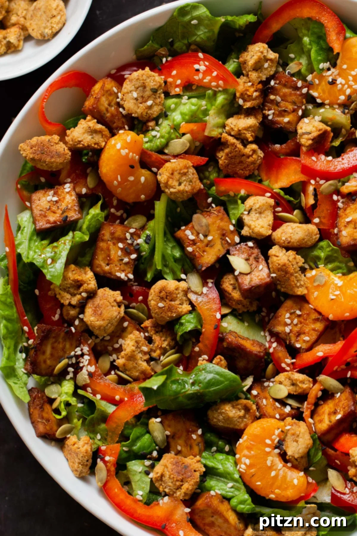 A close-up view of the vegan summer salad, highlighting the texture of the smoky tofu, the golden crunch of the almond flour croutons, and the vibrant colors of the fresh vegetables and orange segments.