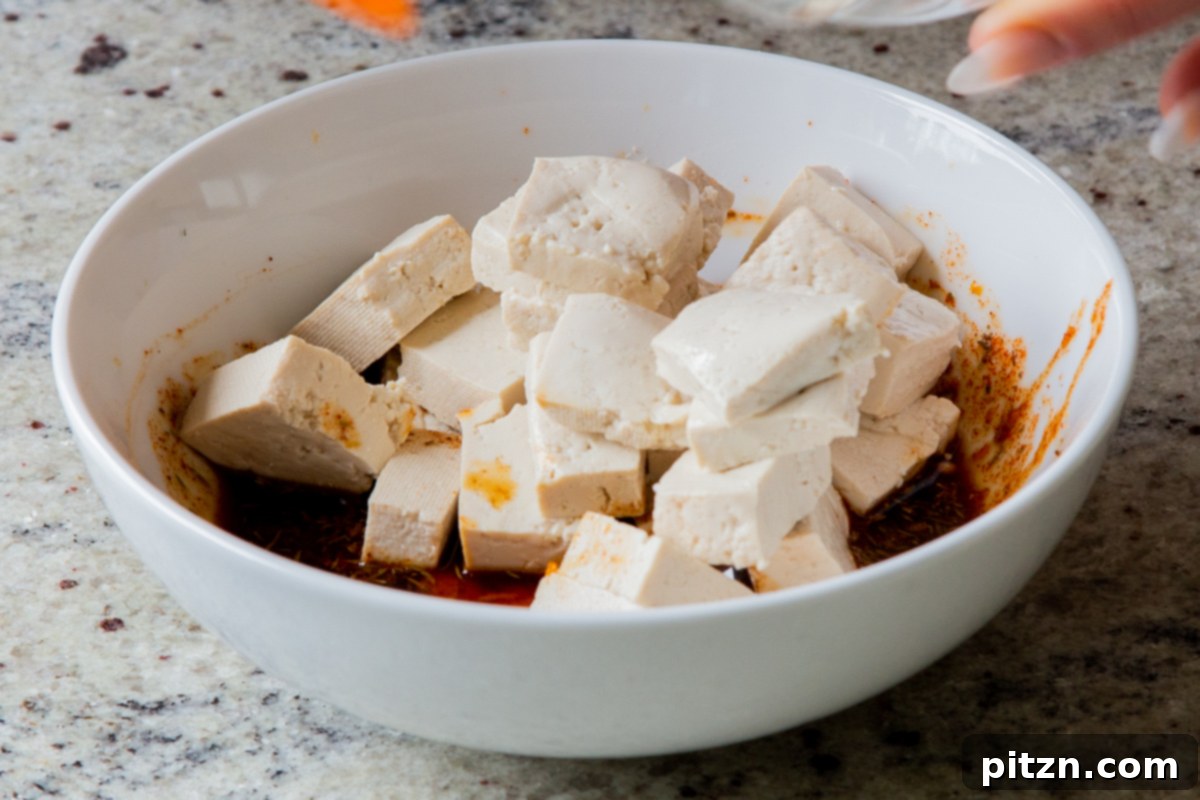 Cubed tofu being gently added to the smoky marinade in a bowl, preparing it to absorb the rich flavors before baking.