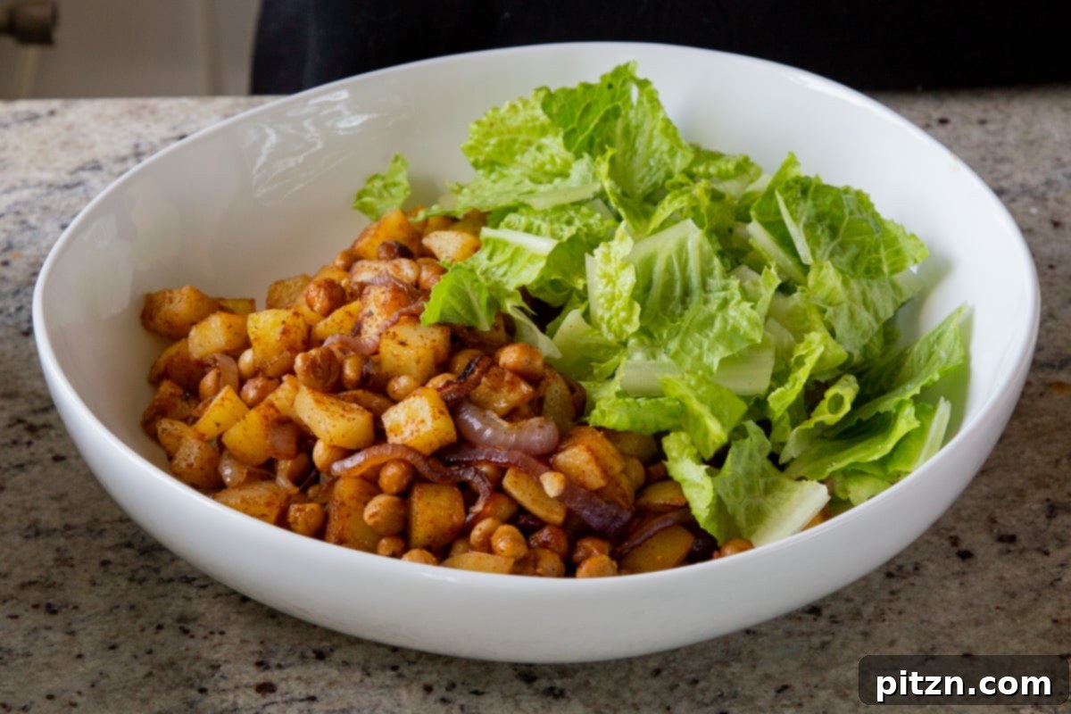 Smoky Chickpea Potato Salad 14 Freshly torn lettuce being added to a bowl containing the roasted BBQ chickpeas, potatoes, and onions.