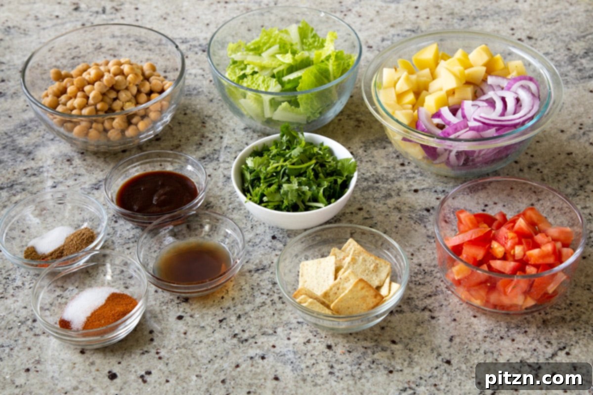Smoky Chickpea Potato Salad 6 An inviting overhead shot of all the individual ingredients for the BBQ chickpea and potato salad laid out on a kitchen counter: roasted chickpeas, potatoes, onions, fresh vegetables, and the BBQ dressing components.