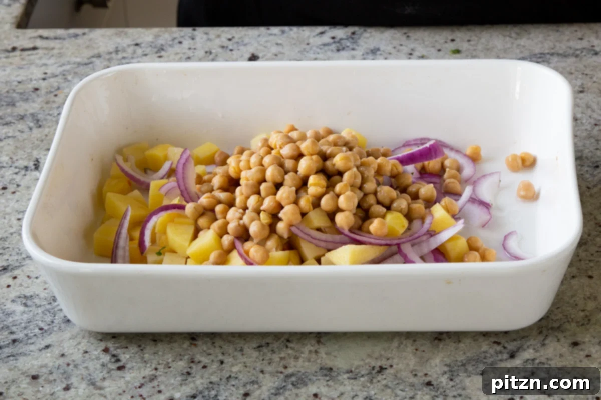 Smoky Chickpea Potato Salad 7 Chickpeas, sliced onions, and cubed potatoes evenly distributed in a baking dish, ready for seasoning.