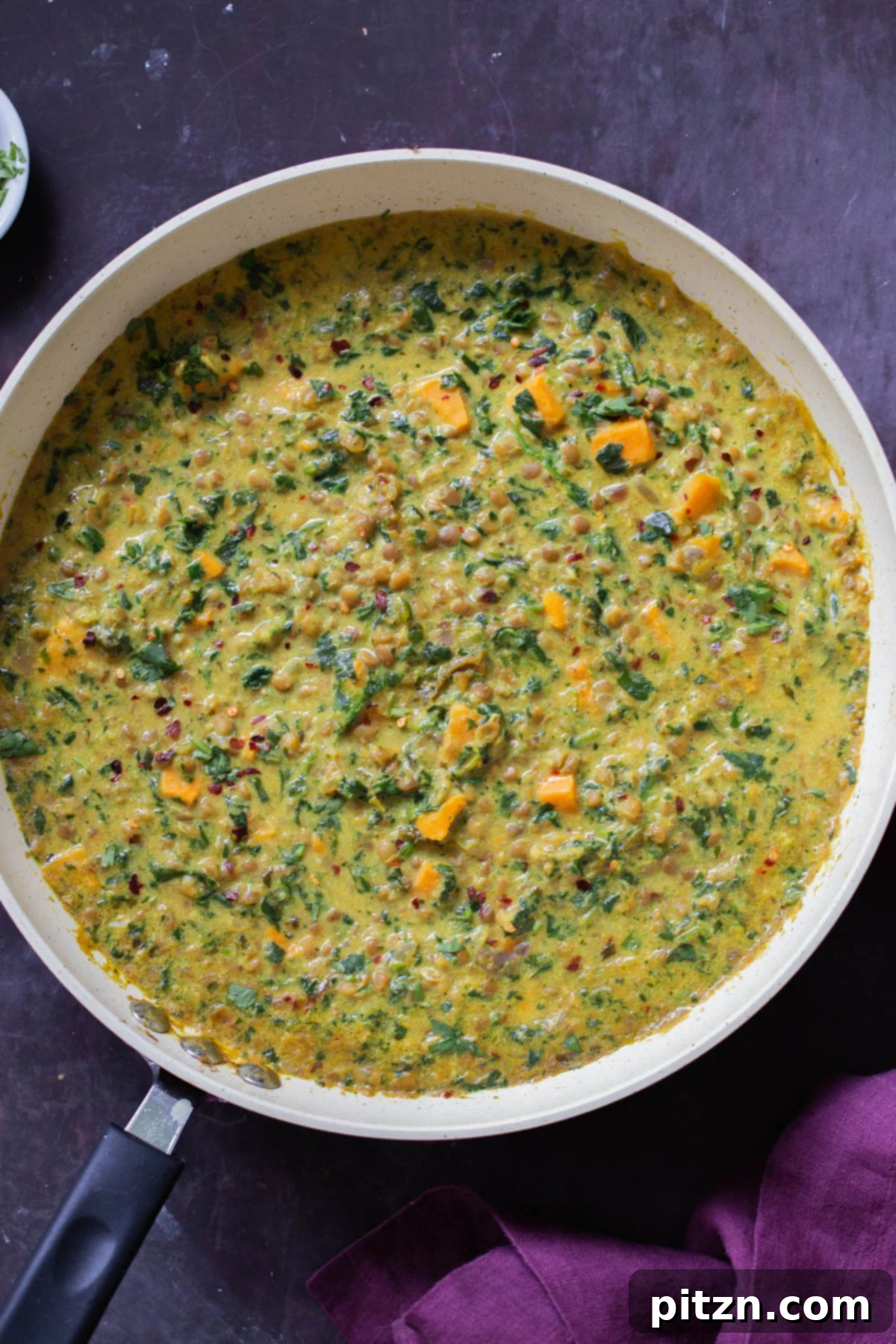 A panful of rich, creamy lentil coconut curry with sweet potatoes on a slate table, ready to be served.