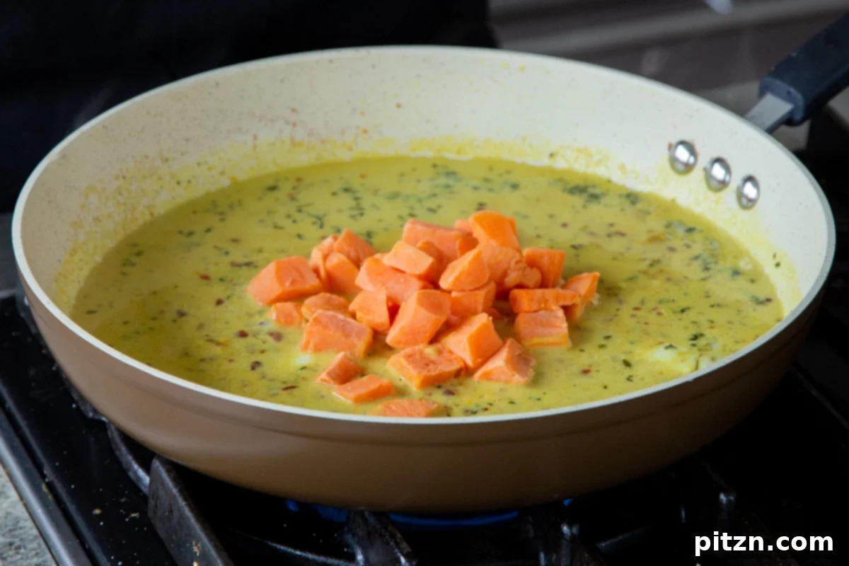 Adding cubed sweet potatoes to the simmering coconut curry sauce in the pan, preparing for cooking.