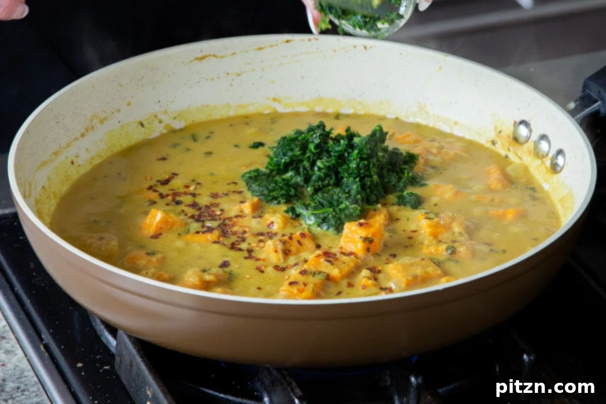 Stirring fresh spinach into the cooked sweet potato and curry sauce in the pan, adding greens to the dish.